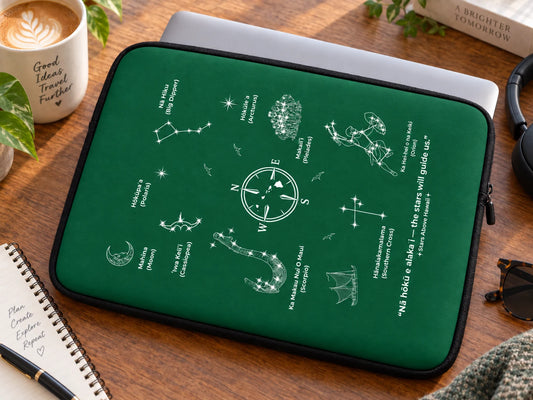 Green Polynesian Star Navigation laptop sleeve beside a silver laptop on a wooden desk with coffee, notebook, and travel accessories